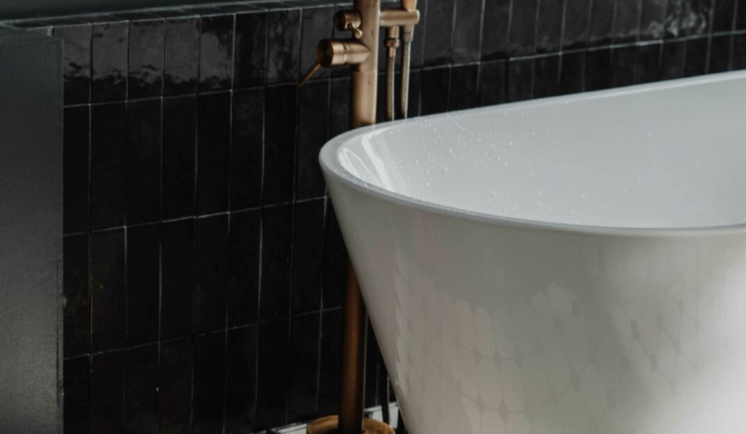 Black bathroom with bath and gold tap detailing